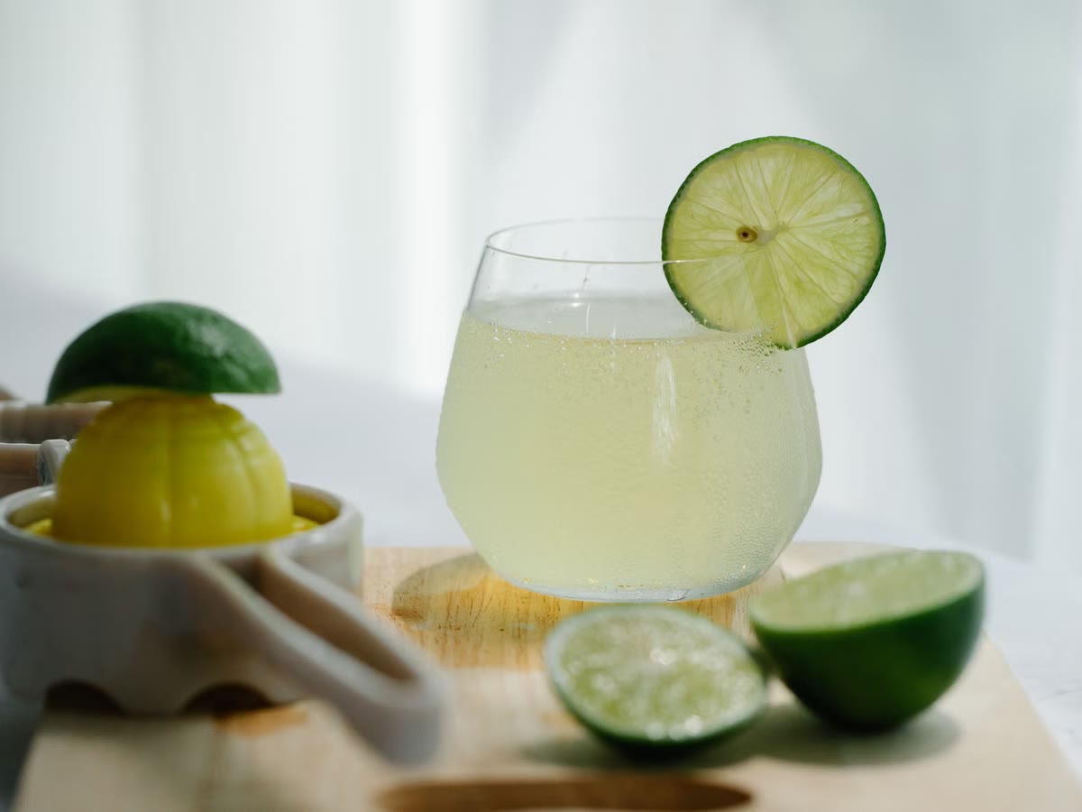 Fresh lime juice in a clear glass beside halved limes and a hand juicer.